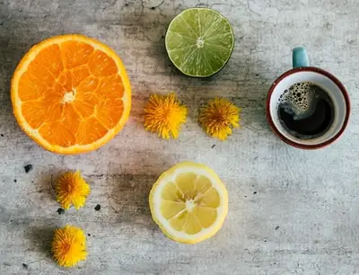 cup of coffee next to half a lime, orange, and lemon with four yellow flowers