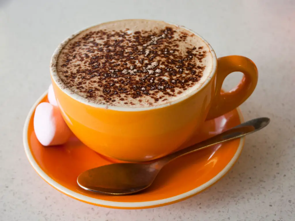 mochaccino coffee in an orange mug and saucer with teaspoon