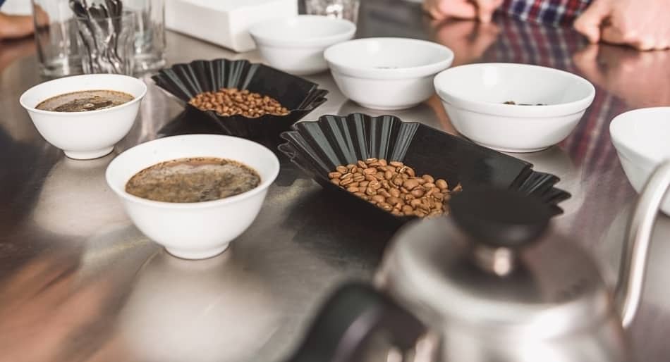 coffee brewing in cupping bowls with whole bean coffee by its side