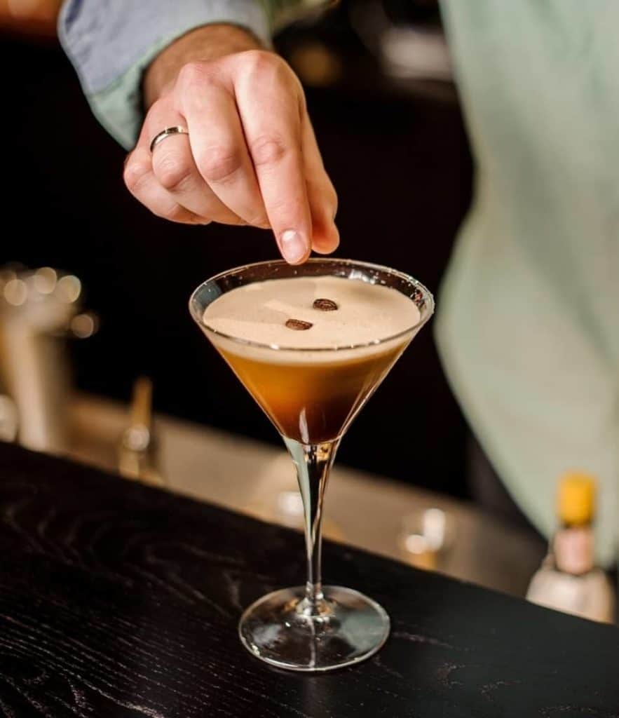 bartender finishing an espresso martini by adding whole coffee beans