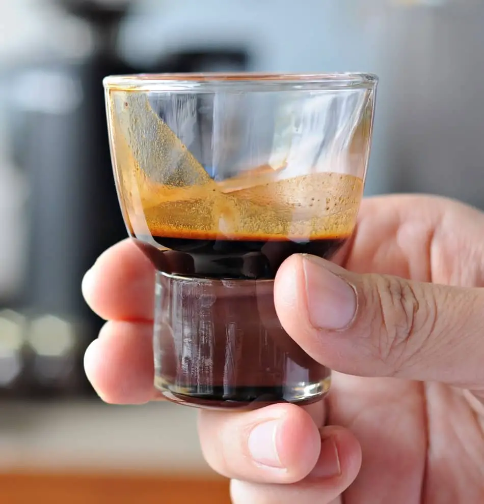 a hand holding a glass of ristretto coffee