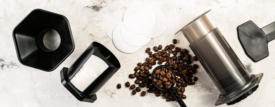 AeroPress with funnel, papers, paper holder, paper filters, stirring paddle, scoop, and whole coffee beans