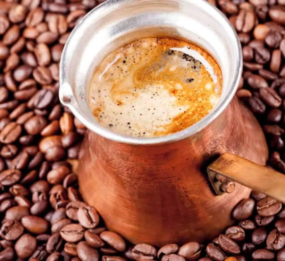 Brewed Turkish coffee in an ibrik sitting on whole coffee beans