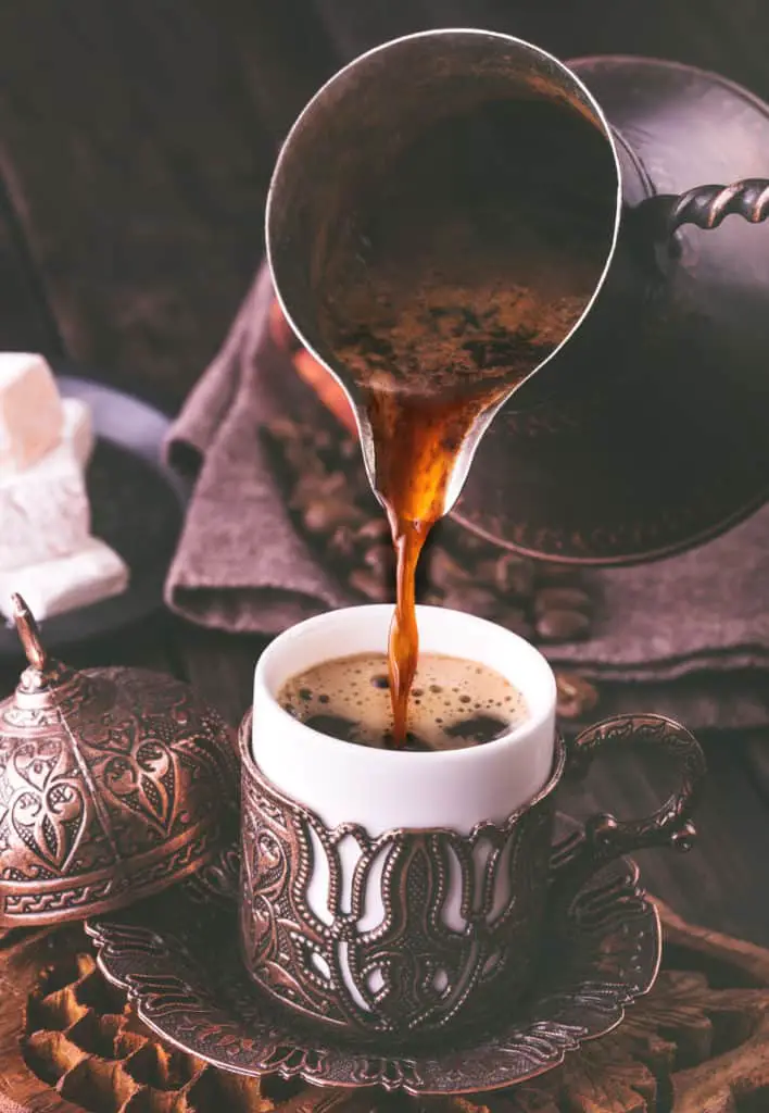 Turkish coffee being poured unfiltered from an ibrik into a traditional Turkish cup