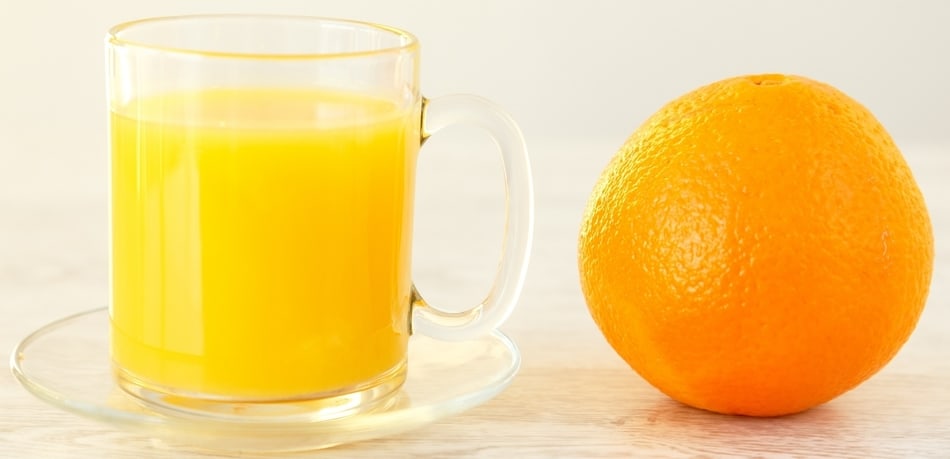 glass of orange juice next to a whole orange